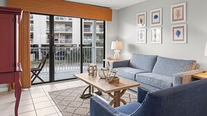 Un soggiorno moderno con un divano grigio, un tavolino in legno e un armadietto rosso. Alle pareti ci sono quadri incorniciati e si vede un balcone con un edificio sullo sfondo.