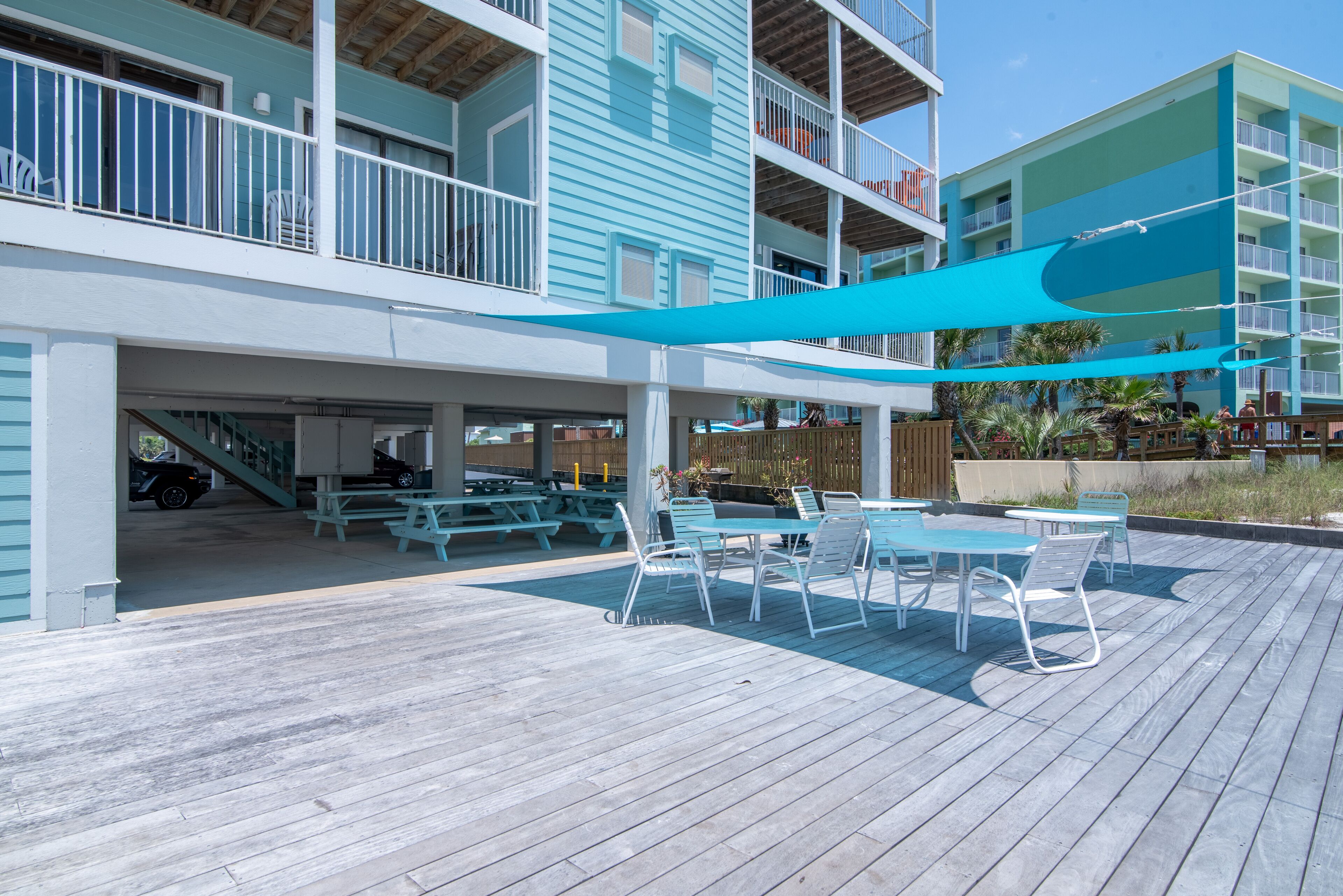 A covered outdoor area with picnic tables and chairs, a car parked inside, and a building with multiple balconies.