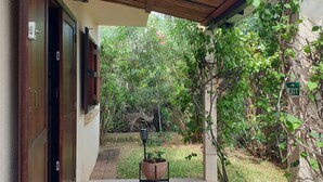 En overdækket terrasse med flisegulv, trædøre og udsigt til en have med en potteplante og et skilt, der angiver en udgang.