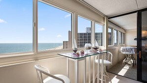 A balcony with a glass table, white chairs, and a view of the beach and ocean.