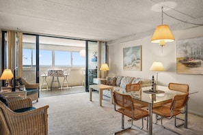A spacious living area with a glass table, wicker chairs, a sofa, and a balcony with a view of the sea. - Atlantis 2 Br/2 Ba oceanfront with outdoor pool (Ocean City)