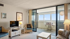 A spacious living room with a television, seating area, and a balcony with a table and chairs.