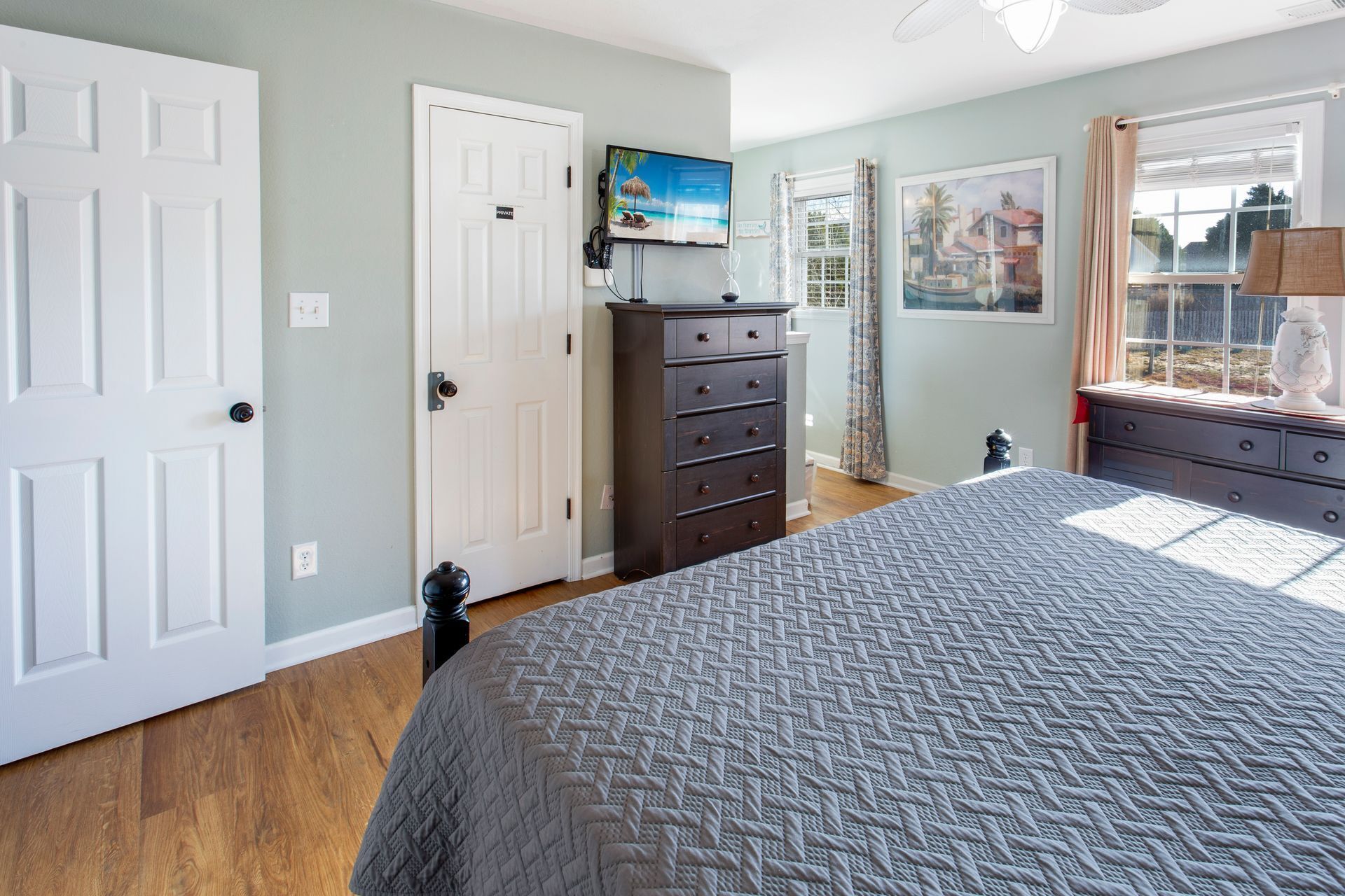 A bedroom with a bed, a dresser, a television, and a window with curtains.