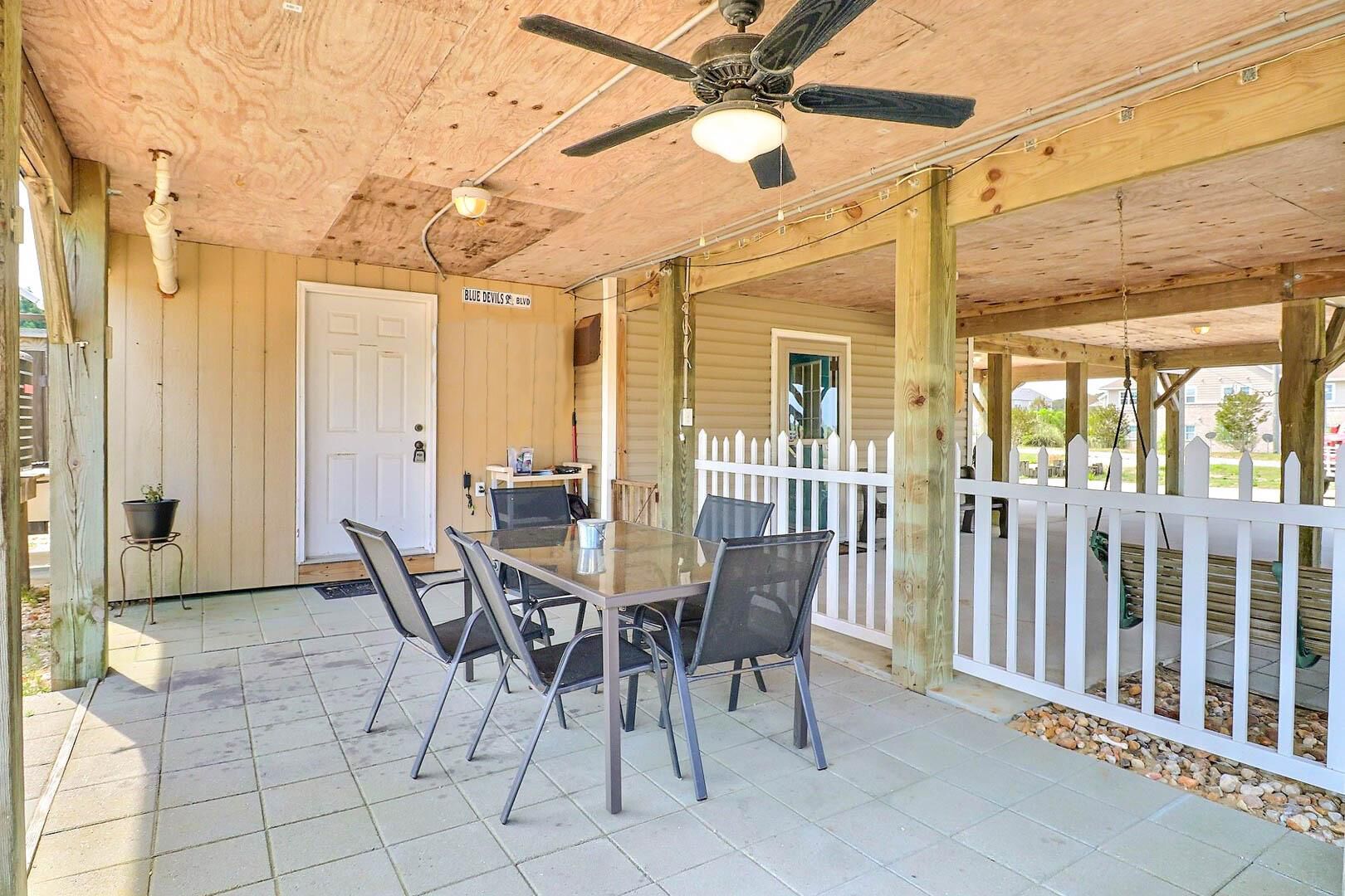 A covered patio with a table and chairs, a ceiling fan, and a white picket fence.