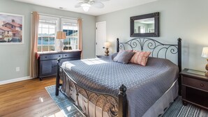 Een slaapkamer met een bed, een dressoir, een nachtkastje, een plafondventilator en een groot raam met gordijnen.