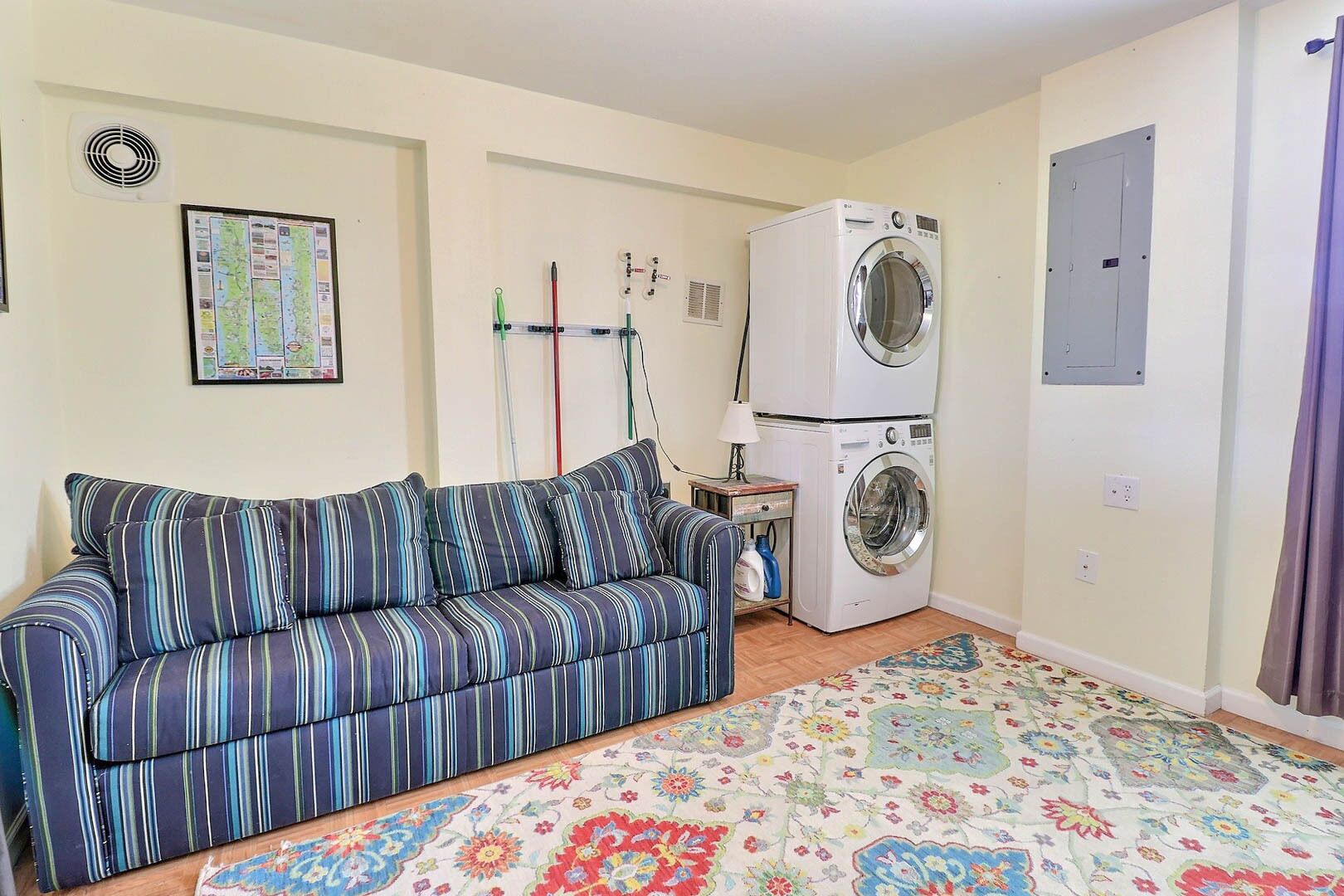 A living room with a striped sofa, a washing machine, a radiator, and a floral rug.