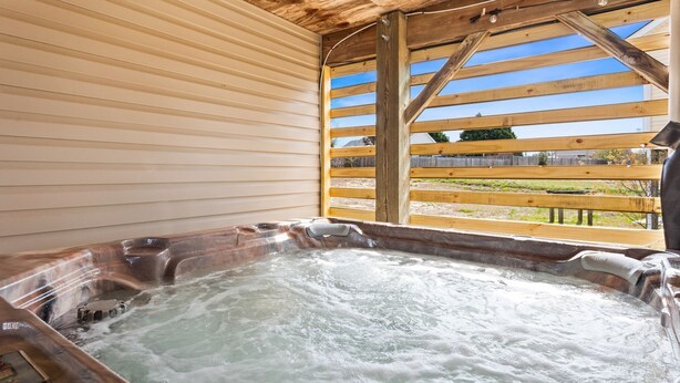 Een hottub met een houten terras en uitzicht op een omheinde tuin.
