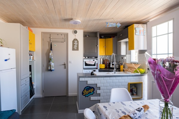 Una cocina compacta con una isla central, una zona de comedor con mesa y una puerta que da a otra habitación.