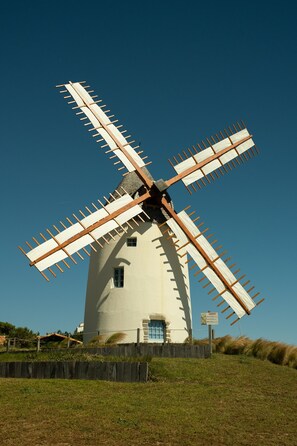 A windmill with a white body and wooden blades, set against a clear blue sky. - The blue jewel of the Vendée coast (Jard-sur-Mer)