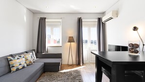 A modern living room with a grey sofa, patterned cushions, a floor lamp, and a dining table with decorative items. - Feel Porto Historic Boutique Flat (Porto)