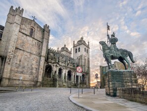 A historic stone building with a statue of a figure on horseback, a no parking sign, and a cobblestone street.