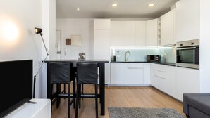 A modern kitchen with white cabinets, a dining area with two chairs, a TV, and a lamp. - Feel Porto Historic Boutique Flat (Porto)