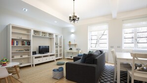 A modern living room with a grey sofa, white entertainment unit, and a dining area with a table and chairs. - Feel Porto Downtown Essence (Porto)