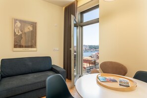 Una habitación moderna con sofá, una mesa de comedor con sillas, una ventana con vista a un paisaje urbano y un cuadro en la pared.