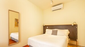 A neatly made bed with a wooden headboard, a bedside lamp, and a wall-mounted air conditioner. - Feel Porto Code al Apartment 0 1 (Porto)