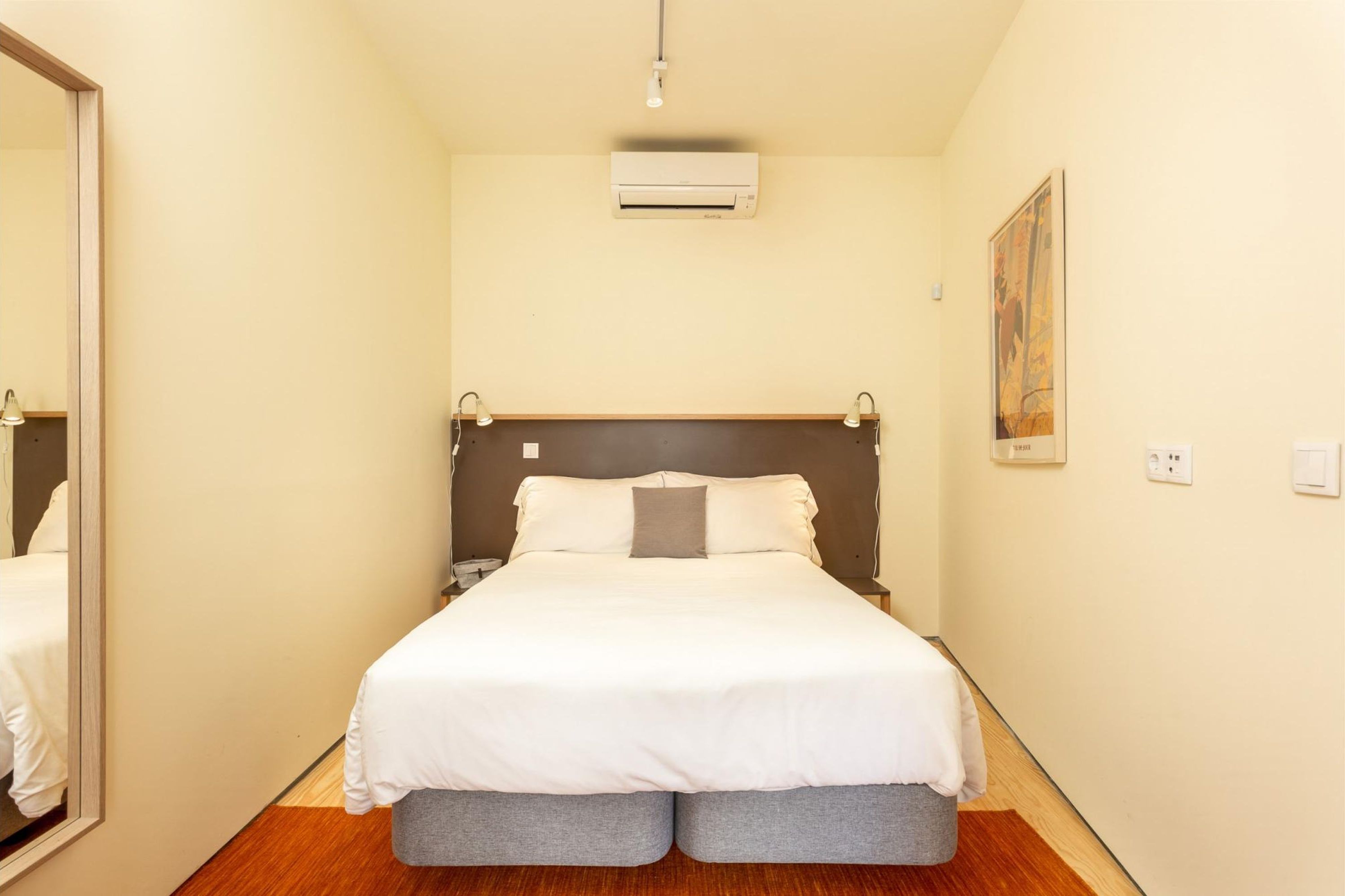 Ein Hotelzimmer mit einem großen Bett, Nachttischen, einem Spiegel, einer Klimaanlage und einem Bild an der Wand.