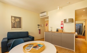Quarto de hotel moderno com sofá, uma mesa de jantar com revistas, uma kitchenette e um extintor de incêndio.