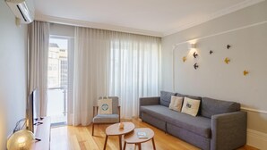 Un saló modern amb un sofà gris, dues taules rodones petites, un televisor i una finestra gran amb cortines.