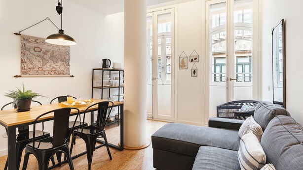 A modern living room with a grey sofa, a wooden dining table, black chairs, a hanging lamp, and a large window with a view of buildings. - Galerias Cashmere Nightlife 302 by Feel Porto (Porto)