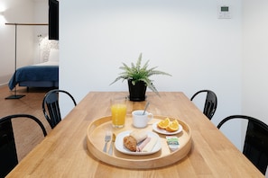 A breakfast tray with croissant, ham, cheese, orange slices, and juice on a wooden table in a room with a bed and a potted plant.