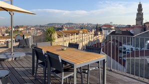 Una terraza en la azotea con mesa y sillas de madera, una planta en maceta y vistas de la ciudad, incluyendo una torre destacada.