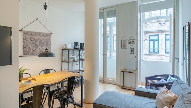 Una sala de estar moderna con una mesa de comedor de madera, sillas negras, un sofá gris y una lámpara colgante negra.