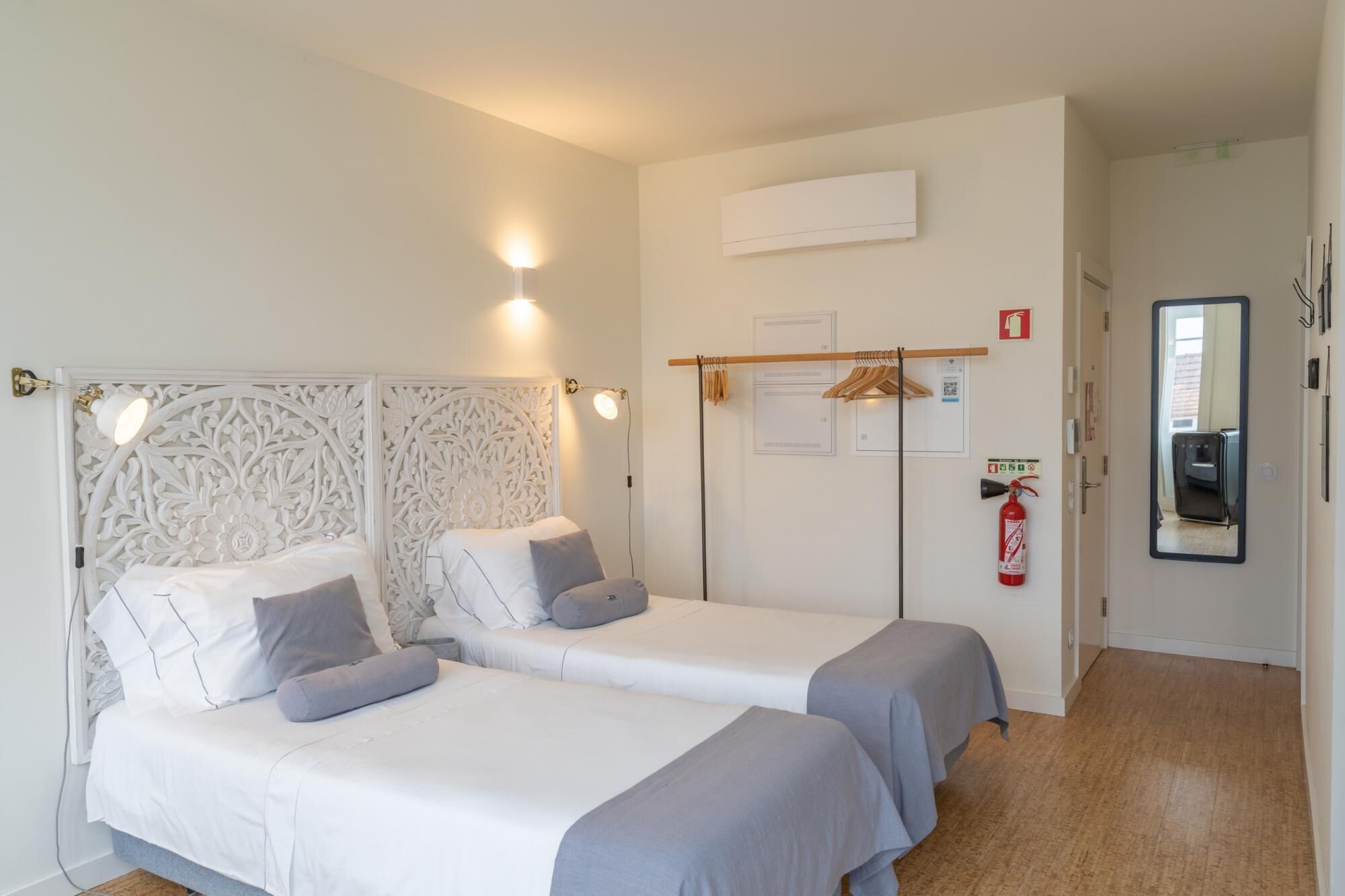 Habitació d'hotel amb dos llits, un armari, un mirall i un extintor.