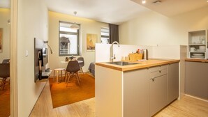 A modern kitchen with a central island, a dining area with chairs, and a view of the outdoors through a window. - Feel Porto Code al Studio 1 2 (Porto)