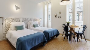 A room with two beds, a dining table with chairs, and a window with a view of buildings. - Galerias Cotton Cozy Nightlife 101 by Feel Porto (Porto)