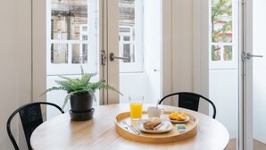 Bandeja de desayuno con cruasanes, zumo de naranja y una planta sobre una mesa junto a una ventana con vista a la ciudad.
