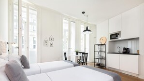 Una habitación moderna y minimalista con dos camas, un pequeño comedor y una kitchenette.