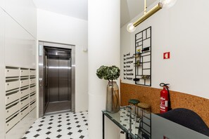 Um elevador moderno, um extintor de incêndio, uma mesa de vidro com uma planta e uma frase motivacional na parede.