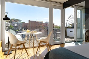 Un balcón con mesa y sillas, un ventanal corredero y vista panorámica de la ciudad.
