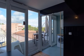 Un balcón con vistas a edificios, una mesa, sillas y una lavadora.