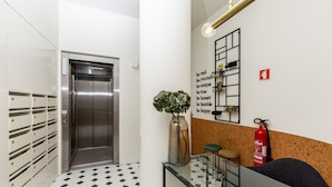 Een moderne lift met een metalen afwerking, een wandplank met diverse spullen, een brandblusser en een vloer met een patroon.