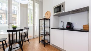 Een moderne keuken met witte kastjes, een zwart aanrecht, een magnetron, een koffiezetapparaat en een houten plank.