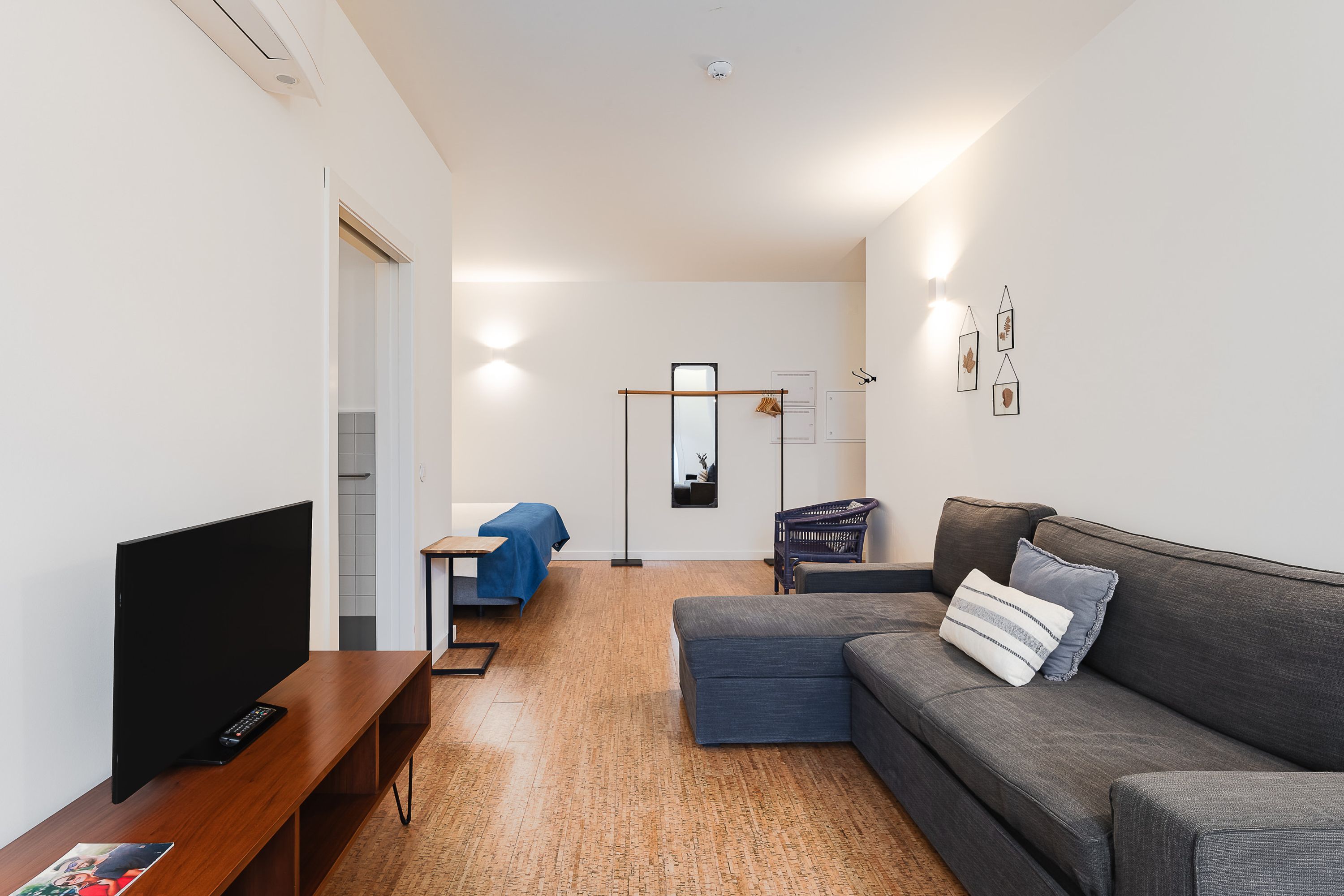 A modern living room with a flat-screen TV, a sofa, a coffee table, and a small table with a blue tablecloth.