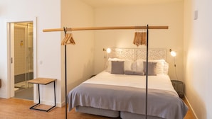 A bedroom with a bed, bedside tables, a hanging rack, and a shower area. - Galerias On Trend Nightlife 203 by Feel Porto (Porto)