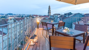 A rooftop terrace with a table and chairs, a large umbrella, and a view of a cityscape including a tower. - Galerias On Trend Nightlife 203 by Feel Porto (Porto)