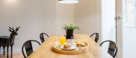 A dining area with a wooden table, black chairs, a tray with breakfast items, a potted plant, and a pendant light.