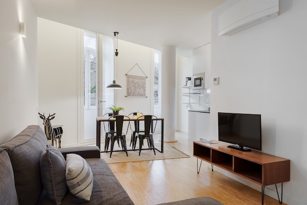 Una sala de estar moderna con sofá, televisor, mesa de comedor, sillas y una cocina equipada.