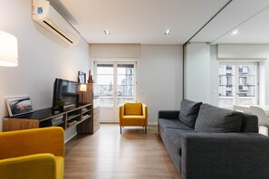 A modern living room with a sofa, a yellow chair, a television, and a bookshelf.