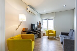 A modern living room with a flat-screen TV, a lamp, and two chairs.