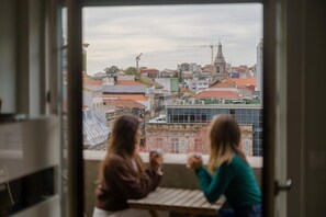 Deux personnes sont assises à une table près d’une fenêtre donnant sur un paysage urbain, avec des immeubles et une église.