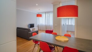 A modern living room with a grey sofa, a dining table with red chairs, and a large red pendant light. - Feel Porto Downtown Harmony (Porto)