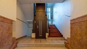 A staircase with marble steps and wooden handrails, leading to a dark door with a vertical handle. - Feel Porto Downtown City Break (Porto)