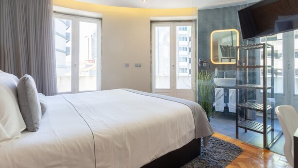 Ein modernes Hotelzimmer mit einem großen Bett, einem Fernseher, einer Duschkabine aus Glas und Blick auf die Stadt.
