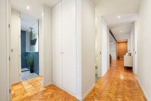 A hallway with wooden flooring, white walls, and a glass door leading to a bathroom with blue tiles. - Feel Porto Ruby Townhouse (Porto)