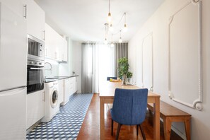 A modern kitchen with white appliances, a dining area with a wooden table and blue chair, and a patterned floor. - Feel Porto Ruby Townhouse (Porto)