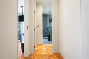 Un couloir doté d’un plancher en bois, de murs blancs et donnant sur un balcon où se trouve une plante en pot.